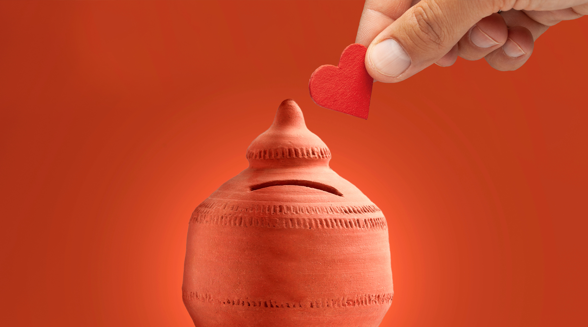 Foto di una mano che mette un cuore in un salvadanaio